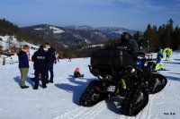 Na pierwszym planie stoi policjant na quadzie, w tle inny policjant rozmawia z narciarzami. Zdjęcie wykonane na stoku narciarskim w Beskidach.