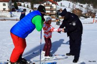 Policjant zakłada dziecku opaskę na rękę, obok stoi opiekun, obydwoje są na nartach. Zdjęcie wykonane na stoku narciarskim w Beskidach.