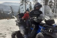 Na pierwszym planie stoi policjant na quadzie i dzieckiem na miejscu pasażera. Zdjęcie wykonane na stoku narciarskim w Beskidach.
