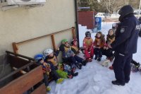 Policjant rozmawia z dziećmi-narciarzami podczas akcji profilaktycznej pod stacją narciarską.