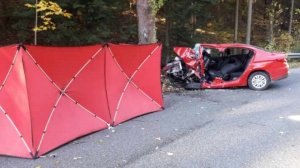 Zdjęcie z miejsca śmiertlenego wypadku. Z prawej strony uszkodzony pojazd osobowy koloru czerwonego, a z lewej czerwony parawan używany przez straż pożarną