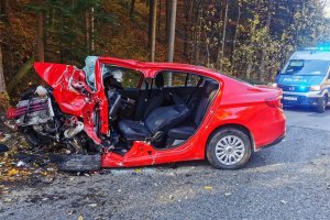 Zdjęcie z miejsca śmiertelnego wypadku. Z lewej strony uszkodzony pojazd osobowy koloru czerwonego, a z prawej radiowóz ruchu drogowego.