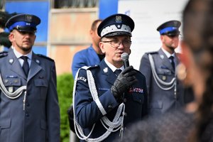 Komendant Wojewódzki Policji w Katowicach podczas przemówienia. Obok niego stoją polcijanci ubrani w mudury galowe.