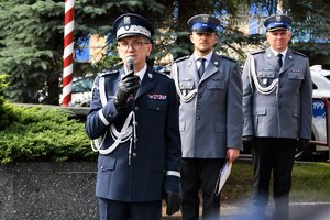 Zdjęcie kolorowe. Widoczny nadinsp Roman Rabsztyn z trzymający mikrofon podczas uroczystości przed budynkiem komendy wojewódzkiej policji, w tle dwaj umundurowani policjanci