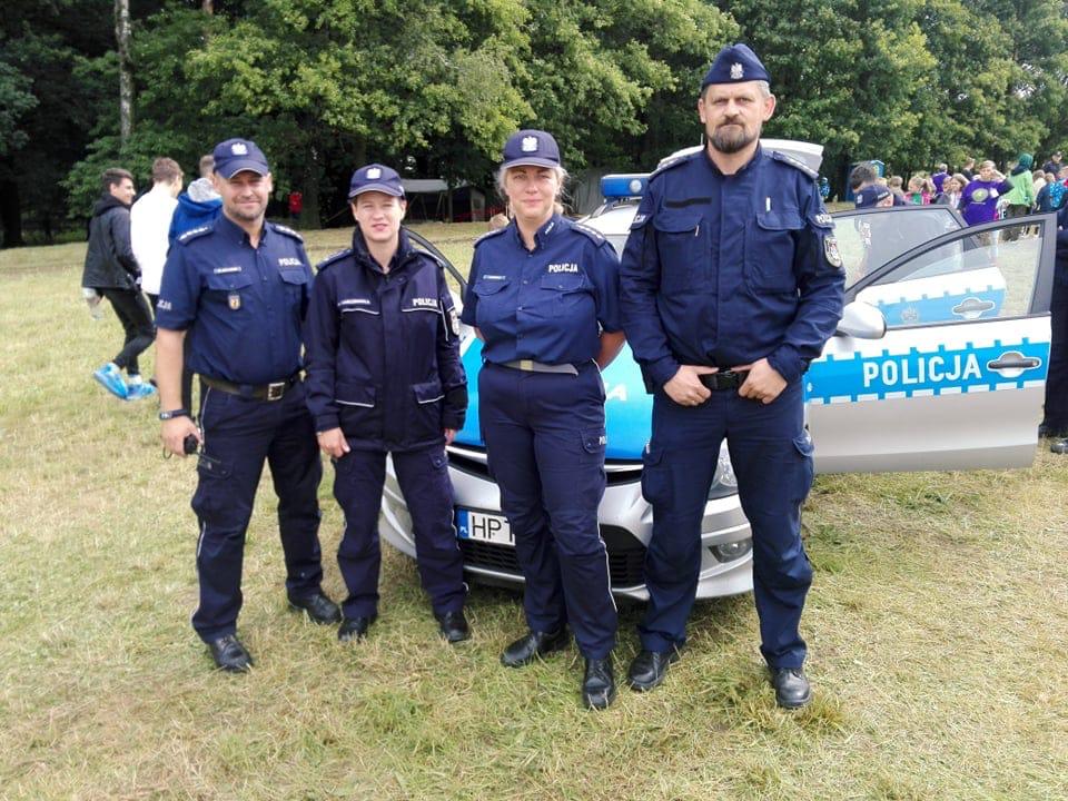 Policjanci obecni na zlocie stoją na tle radiowozu.