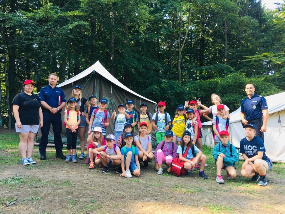 Policjanci harcerze wspólnie na tle harcerskich namiotów.