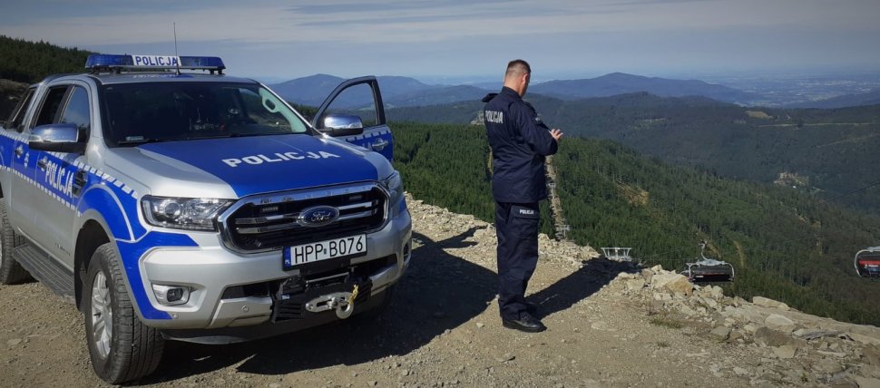 Policjant stoi przy radiowozie. W tle Beskid Śląski