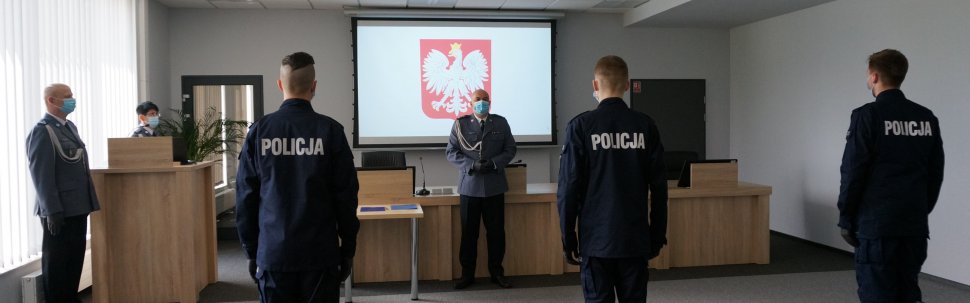 Policjanci w mundurach stoją z prawymi ramionami podniesionymi do góry i powtarzają za przełożonym słowa ślubowania.