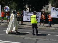 Policjant stoi na ulicy, na chodniku młodzież z bielskich szkół z transparentami