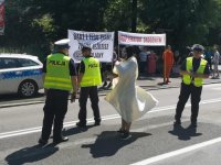 Policjanci i uczestnik akcji przebrany za kostuchę stoją na jezdni, na chodniku młodzież z transparentami