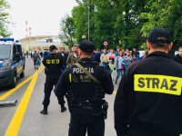 Policjanci i strażacy zabezpieczają rejon stadionu, w tle tłum ludzi.