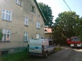 Miejsce pożaru kamienicy, przy budynku stoją wozy straży pożarnej i Policji.