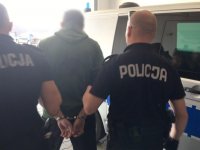 Policjanci prowadzą osobę zatrzymaną do radiowozu.