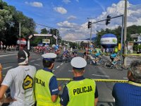 Policjanci zabezpieczają trasę przejazdu, w tle peleton kolarski.