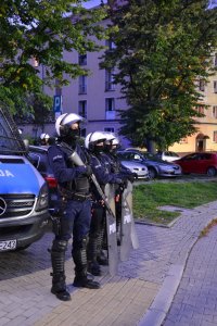 Policjant z długą bronią stoi w kordonie.