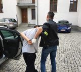 Policjant prowadzi podejrzanego zakutego w kajdanki do prokuratury.