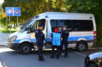 Policjanci wraz ze stewardem rozmawiają z jednym z kibiców przy radiowozie.