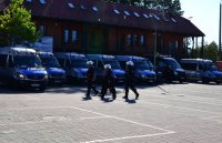 Policjanci prowadzą zatrzymanego do radiowozu. W tle policyjne busy.
