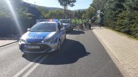 Radiowozy policyjne stoją na ulicy. W tle rowerzyści.
