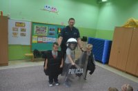 Policjant z trójką dzieci ubraną w policyjne wyposażenie stoi w klasie.