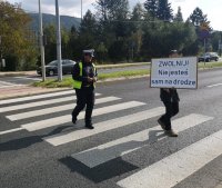 Pieszy przechodzi przez jezdnie z napisem nie jesteś sam na drodze, zwolnij.
