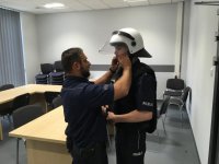 Policjant zakłada kask policyjny na głowę mężczyzny.