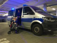 Mężczyzna na wózku inwalidzkim stoi obok radiowozu.