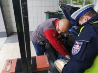 Diagnosta podłącza urządzenie do samochodu, z boku stoi policjant w mundurze.