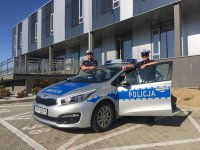 St. sierż. Kamil Foszcz i sierż. Krzysztof Jarzyna stoją przy oznakowanym radiowozie przed budynkiem Komendy Miejskiej Policji w Bielsku-Białej.