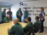 Mężczyzna w więziennym uniformie stoi z założonymi alko-goglami. Reszta skazanym się przygląda. Obok policjantka omawia ich działanie.