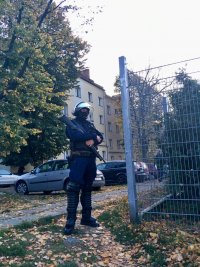 Policjant oddziałów prewencji stoi ze strzelbą przy ogrodzeniu stadionu piłkarskiego.