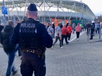 Dowódca policyjnej drużyny obserwuje kibiców idących w kierunku wejścia na stadion piłkarski.