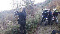 Leśna droga. Policjanci stoją na motocyklach, na pierwszym planie strażnik leśny wykonuje fotografię.