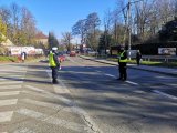 Policjanci z ruchu drogowego stoją w rejonie drogi dojazdowej do cmentarza.