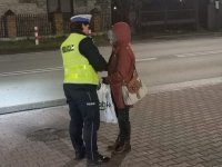 Policjantka zakłada pieszej opaskę odblaskową.