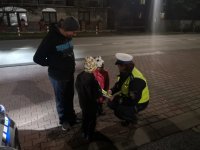 Policjantka rozmawia z dziećmi, w ręku trzyma plik opasek odblaskowych, które rozdaje pieszym.