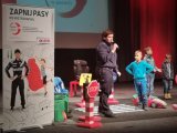 Policjantka na scenie stoi przy inscenizacji przejścia dla pieszych, obok dziecko słucha prelekcji.