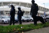 Policjanci, jeden z psem służbowym obserwują okolice stadionu piłkarskiego.