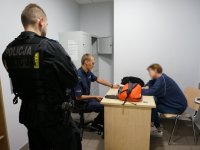 Policjanci rozmawiają z zatrzymaną kobietą, która siedzi przy biurku.