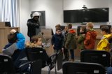 Dzieci podchodzą do policjanta, którzy trzyma przezroczystą tarczę.