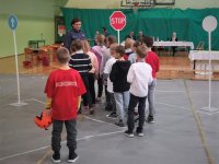 Dzieci podchodzą do policjantki. Wszyscy znajdują się na sali gimnastycznej, gdzie trwa turniej wiedzy o ruchu drogowym.