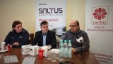 Policjantka, przedstawiciel firmy ubezpieczeniowej i członek Cariatsu siedzą przy stole prezydialnym podczas spotkania.