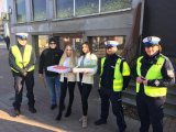 Policjanci i uczestnicy akcji profilaktycznej stoją przy przejściu dla pieszych.