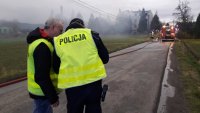 Dwaj policjanci rozmawiają ze sobą. Na drugim planie budynek, z którego wydobywa się dym.