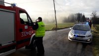 Policjant stoi przy wozie strażackim. Rozmawia z jednym ze strażaków.