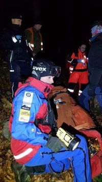 Policjanci i ratownicy GOPR udzielają transportują poszkodowanego na noszach.