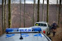 Wozy Policji i Straży Leśnej stoją na leśnej drodze.