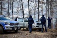 Policjanci stoją przy samochodach. Jeden z nich spogląda przez lornetkę.