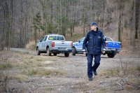 Policjant idzie w leśną drogą. W tle pojazdy Policji i Straży Leśnej.