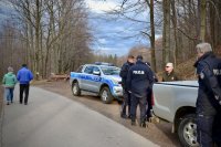 Policjanci i Strażnik Leśny wychodzą z samochodów. Drogą idą turyści.